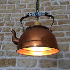 an old tea kettle hanging from a brick wall with a light on it's side