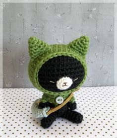 a crocheted black and green cat sitting on top of a white tablecloth