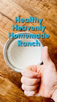 a hand holding a bowl of ranch dressing on top of a wooden table with the words healthy heavenly homemade ranch