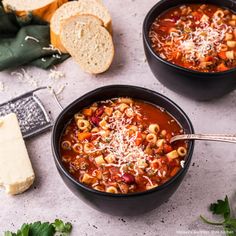 two bowls of pasta soup with bread and parmesan cheese on the side for garnish