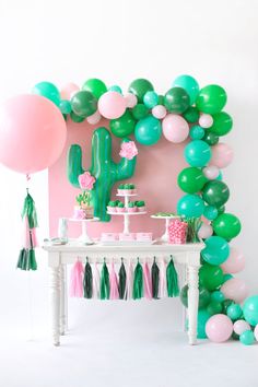 a table topped with lots of balloons next to a wall covered in green and pink