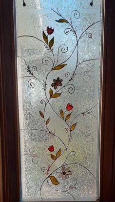 a glass window with flowers and vines on it's side, in front of a door