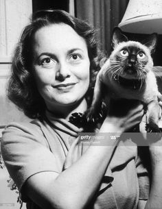 a woman holding a cat in her arms and looking at the camera with an excited look on her face