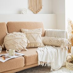 a couch with pillows and blankets on it in front of a window, next to a plant