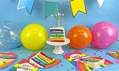 a birthday cake surrounded by balloons and confetti on a blue table with streamers