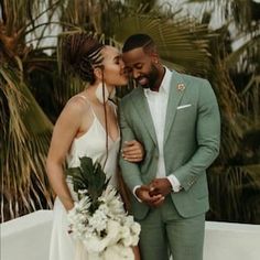 a bride and groom standing next to each other with palm trees in the back ground