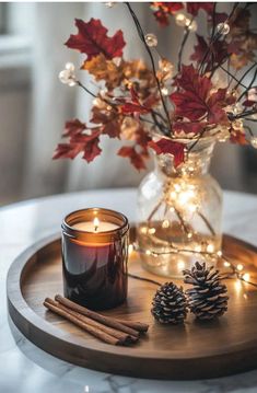 a wooden tray topped with a candle and some pine cones on top of a table