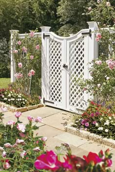 a white garden gate surrounded by flowers and greenery