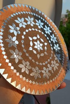 a hand holding a metal plate with designs on it