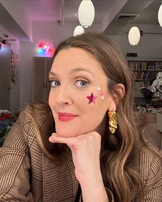 a woman with stars painted on her face sitting in front of a book shelf and looking at the camera