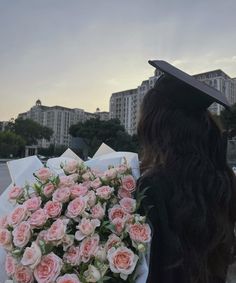 a woman wearing a graduation cap and gown holding a bouquet of flowers in front of buildings