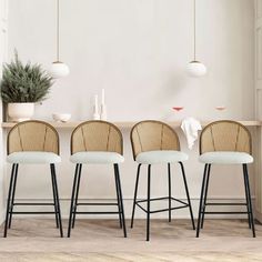 four stools in front of a white wall with plants on the table and two hanging lights above them