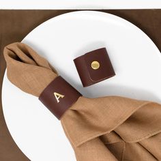 a white plate topped with a brown napkin and a leather cuff on top of it