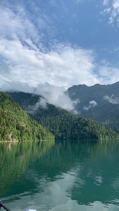 there is a boat that is on the water in front of some mountains and clouds