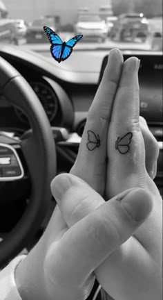 two fingers with butterfly tattoos on them in front of the steering wheel of a car