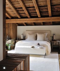 a large bed sitting under a wooden ceiling next to a white rug on top of a hard wood floor