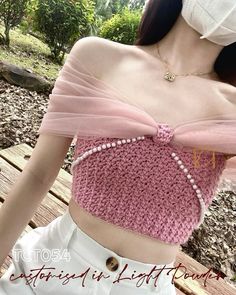 a woman wearing a pink crop top with pearls on the bottom and an attached neckline