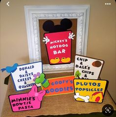 mickey mouse's hot dog bar sign and other signs on display in front of a frame