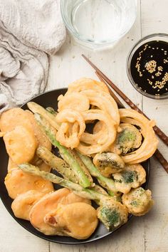 a black plate topped with pasta and vegetables next to chopsticks on a white table