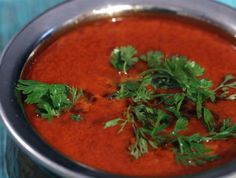 a metal bowl filled with red sauce and garnished with parsley