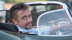 a man sitting in the driver's seat of a green sports car looking at the camera