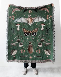 a woman holding up a green blanket with an image of bats and mushrooms on it