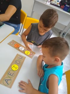 two young boys sitting at a table playing with letters