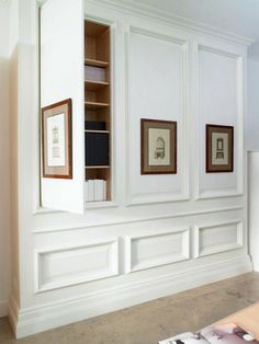 an empty room with white paneling and framed pictures on the wall, along with bookshelves