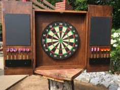 a wooden box with darts in it sitting on top of a tree stump next to a fence