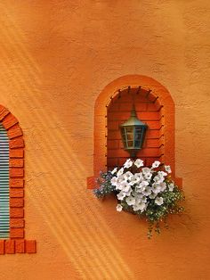 an orange wall with flowers and a lamp on the window sill in front of it