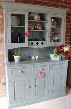 an old china cabinet painted gray with pink hearts on the front and bottom, along with two potted plants