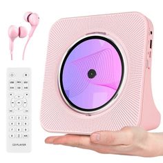 a hand holding a pink speaker with headphones on it and a remote control next to it