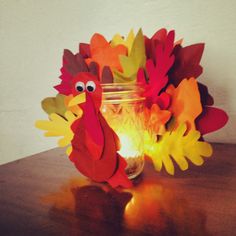 a glass jar filled with paper turkeys sitting on top of a table next to a lit candle