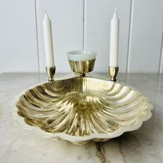 a gold plate with two candles on it and another candle holder in the middle, sitting on a marble countertop