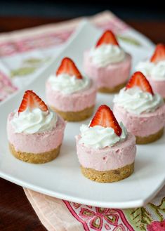 mini strawberry cheesecakes on a white plate with whipped cream and fresh strawberries