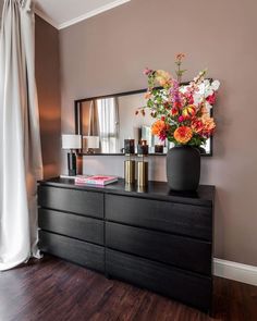 a vase with flowers on top of a dresser next to a mirror and lamp in a room