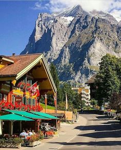 people are sitting at tables in front of a building with mountains in the back ground