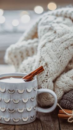 a white mug with cinnamon sticks in it sitting on a table next to a pile of blankets