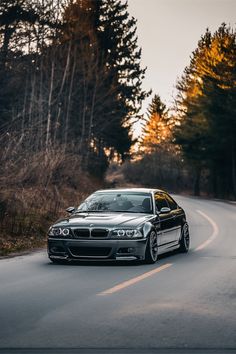 a silver car driving down a road next to trees