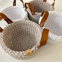 three woven baskets with leather handles on a white table top, one is brown and the other is gray