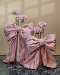 three vases with pink flowers in them on a marble floor and one has a bow