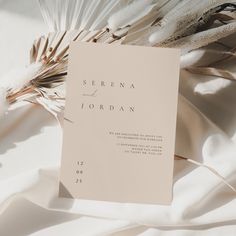 a white wedding card with the word serena and jordan printed on it next to some feathers