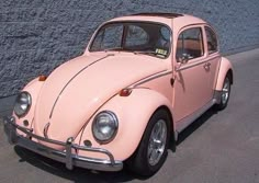 an old pink beetle parked in front of a stone wall