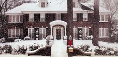 a large red brick house with snow falling on it's roof and trees in the front yard