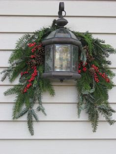 a lantern hanging from the side of a house decorated with greenery and red berries