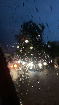 rain is pouring down on the windshield of a car as traffic passes by at night