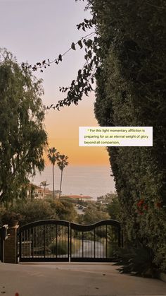 an iron gate with a quote written on it in front of trees and the ocean