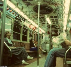 two people sitting on a subway car with graffiti all over the walls and flooring