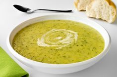 a white bowl filled with broccoli soup next to bread