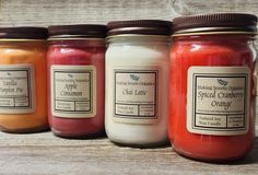 four jars filled with candles sitting on top of a wooden table